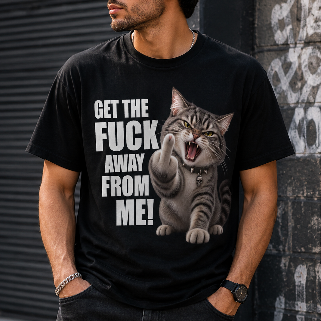 A man wearing a black graphic t-shirt with a bold design featuring a grinning cat giving a middle finger and the text 'GET THE FUCK AWAY FROM ME!'. The man is posing outdoors against a dark gray wall and metal shutter.