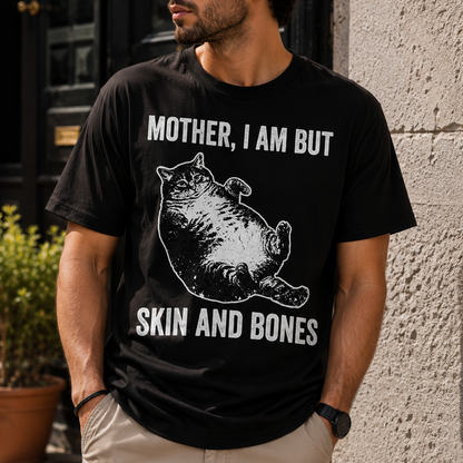 A man wearing a black graphic t-shirt with a white print that reads 'MOTHER, I AM BUT SKIN AND BONES' alongside a cartoon cat illustration, standing outdoors against a stone wall.